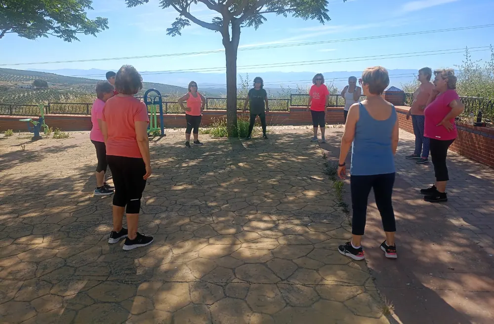 Grupo de alumnas en círculo a la sombra de un árbol, estirando al aire libre con vistas al campo