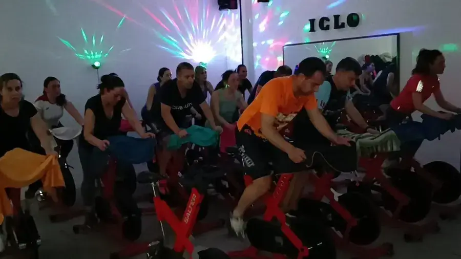 Clase de spinning en Loles Jiménez GYM & PILATES: un grupo de socias y socios pedaleando en bicicletas rojas con luces de colores en la pared